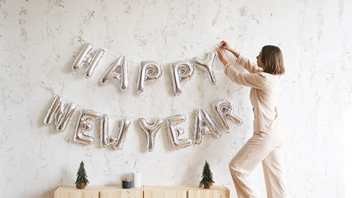 Femme accrochant une banderole bonne année sur un mur blanc pour symboliser les bonnes résolutions à prendre
