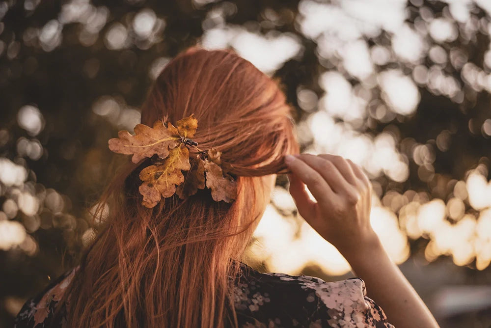 Femme de dos aux cheveux cuivrés décorés de feuilles d’automne pour illustrer la coloration végétale