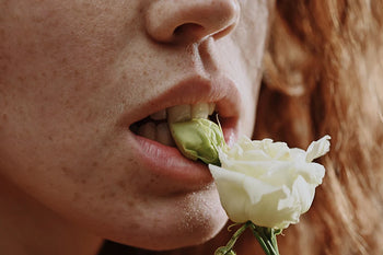 Bouche de femme rousse mordant une rose blanche dans une ambiance sensuelle pour illustrer les aphrodisiaques naturels.