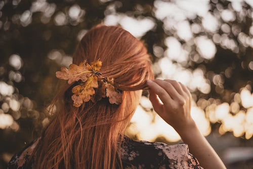 Femme de dos aux cheveux cuivrés décorés de feuilles d’automne pour illustrer la coloration végétale
