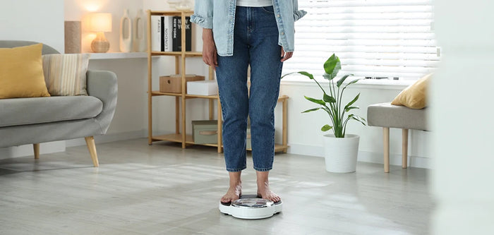 Femme se pesant sur une balance à la maison, illustrant la ménopause et la prise de poids